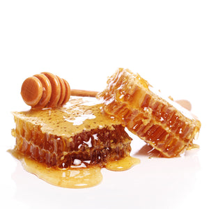 Pieces of raw cut honeycomb dripping with honey, with a wooden dipper